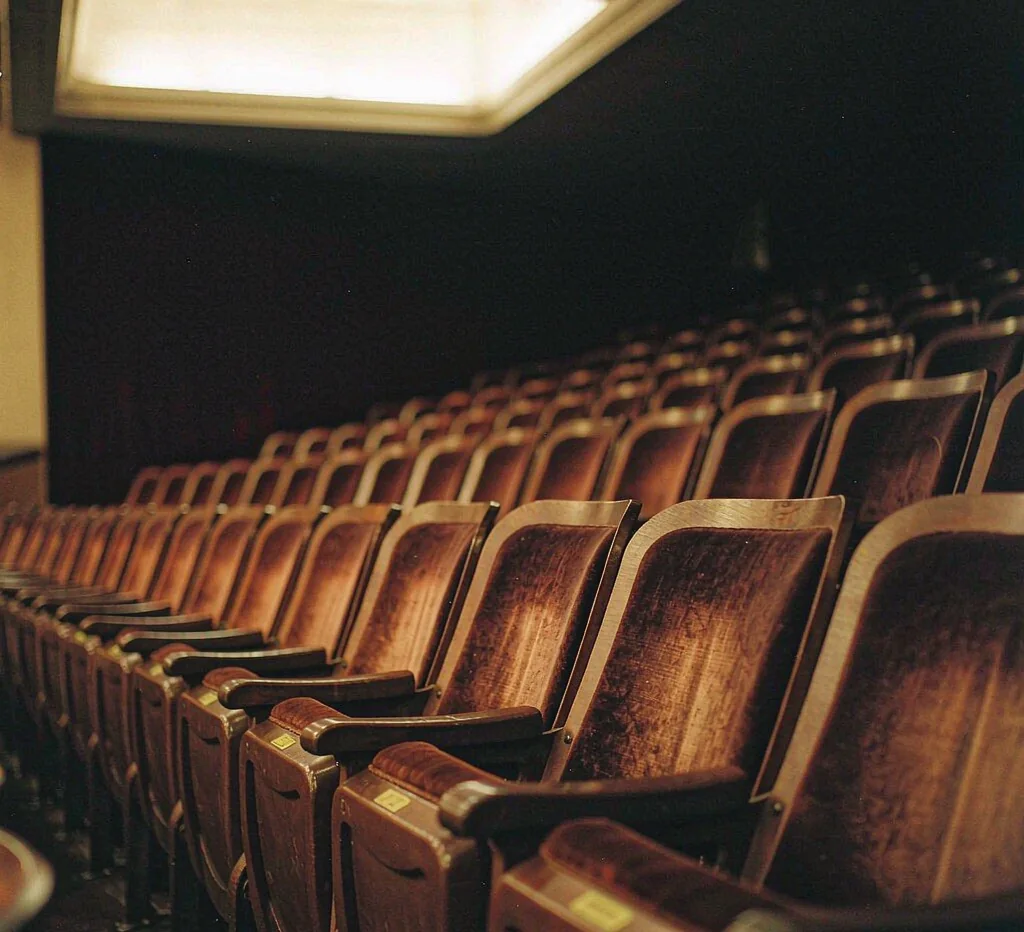 Rows of empty burgundy velvet cinema seats lit by warm amber light