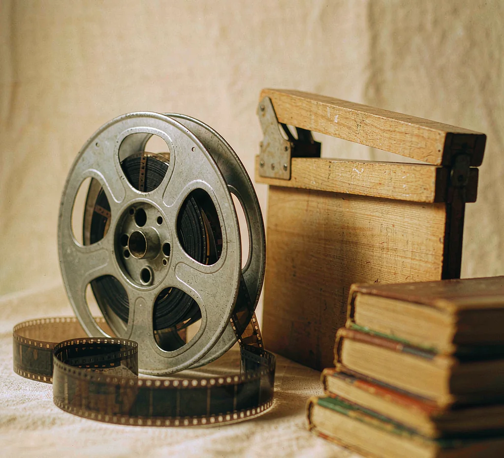 A vintage film reel, a wooden clapperboard and a stack of old hardcover books on cream linen